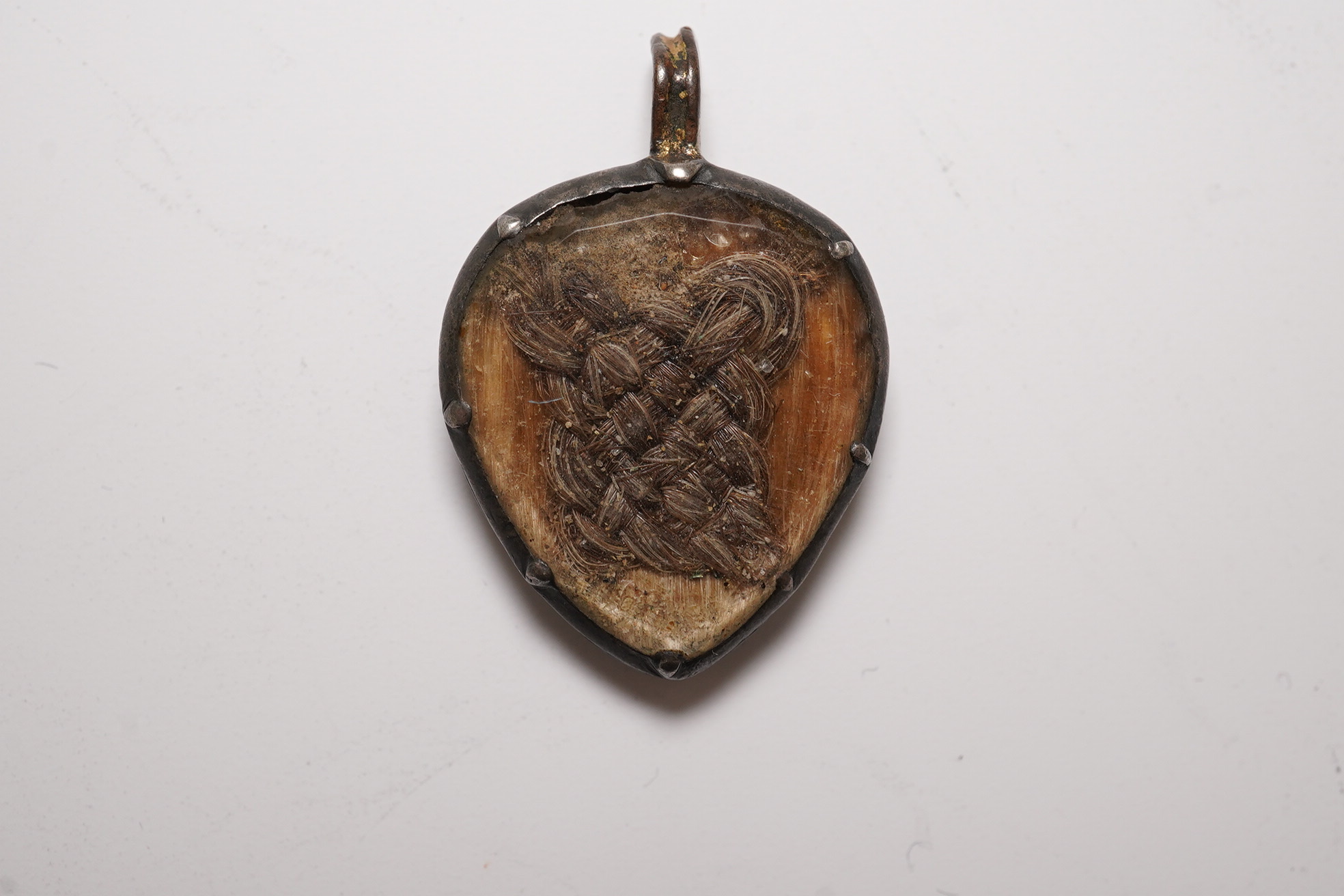 An 18th century gilt metal heart shaped mourning pendant, with engraved inscription, 'CARna DERBY DIED DEC 11th, 1762' and plaited hair beneath a glazed panel verso, 27mm.